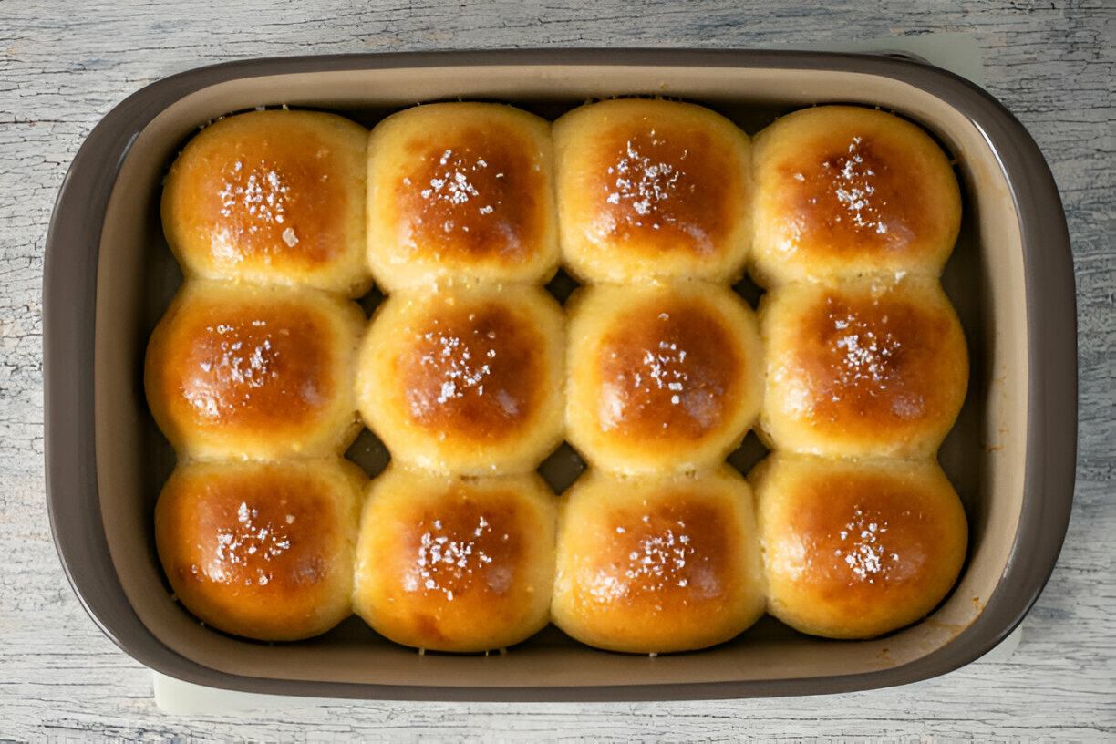 A freshly baked tray of golden brown dinner rolls topped with coarse salt.