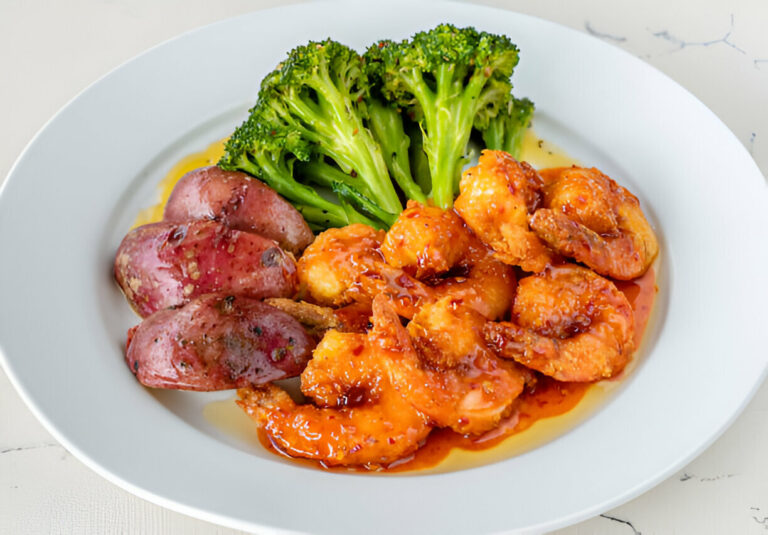 A plate of shrimp in a sweet and spicy sauce served with broccoli and roasted red potatoes.