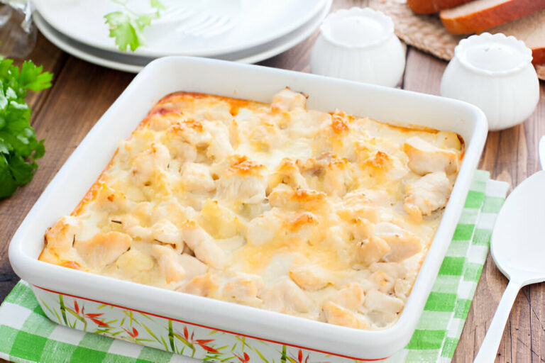 A baked chicken casserole in a white dish on a green checked cloth, surrounded by plates and bread.