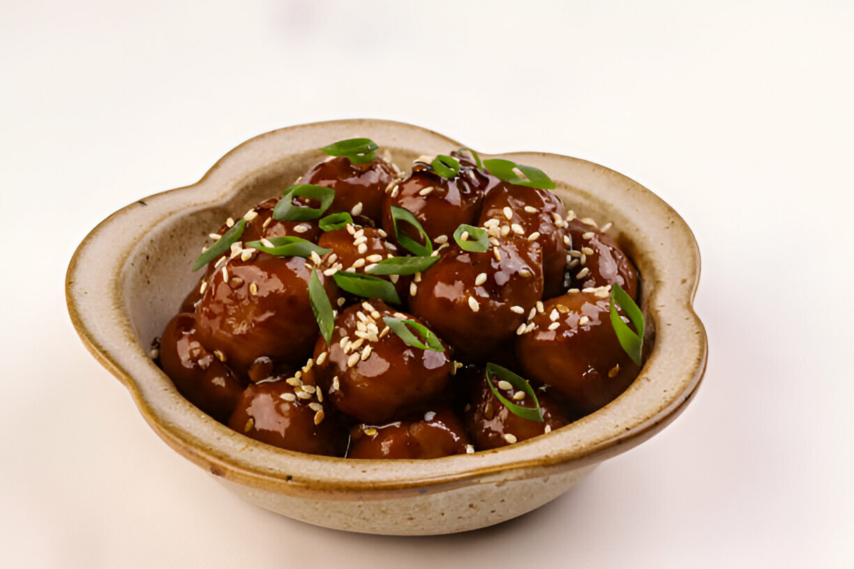 A bowl of glazed meatballs garnished with green onions and sesame seeds.