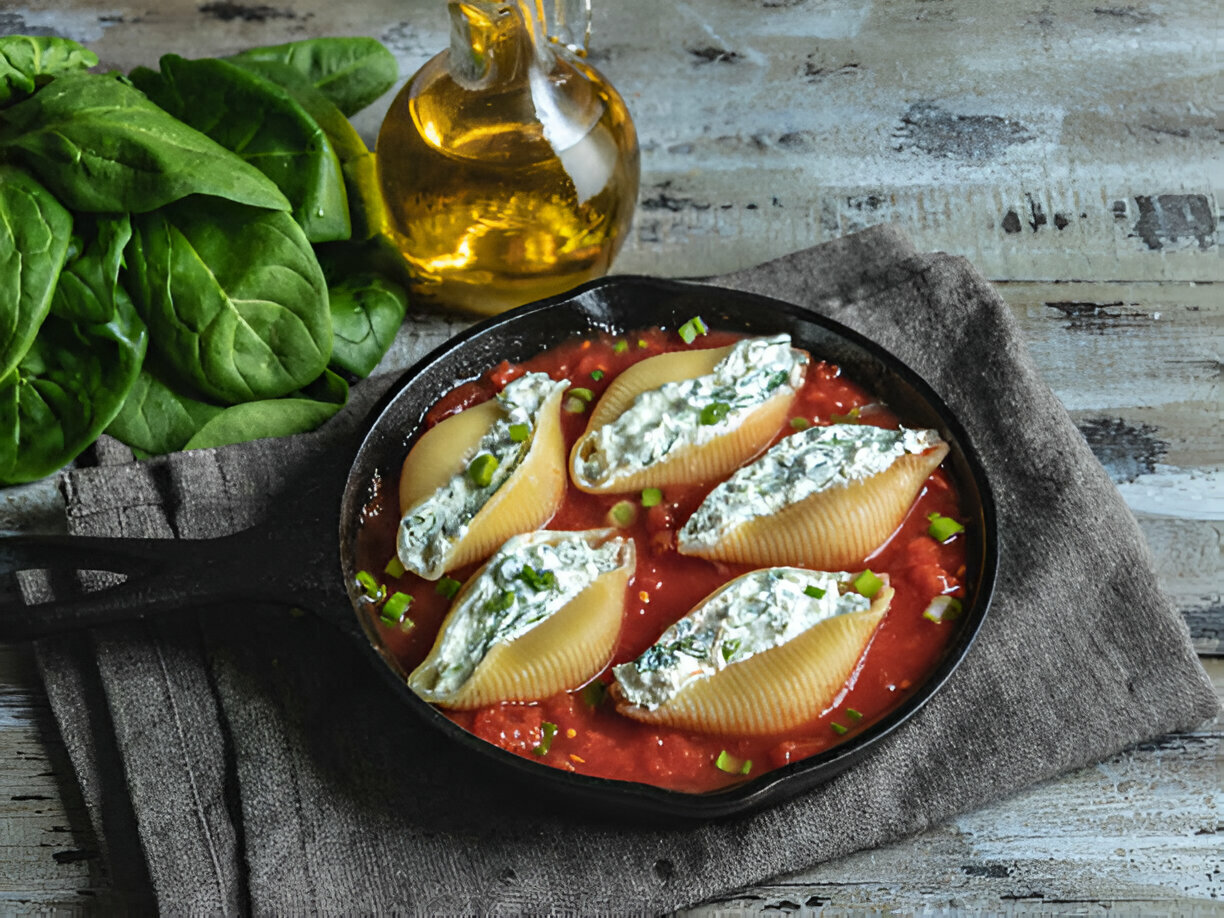 Stuffed pasta shells in a cast iron skillet with tomato sauce and spinach leaves in the background