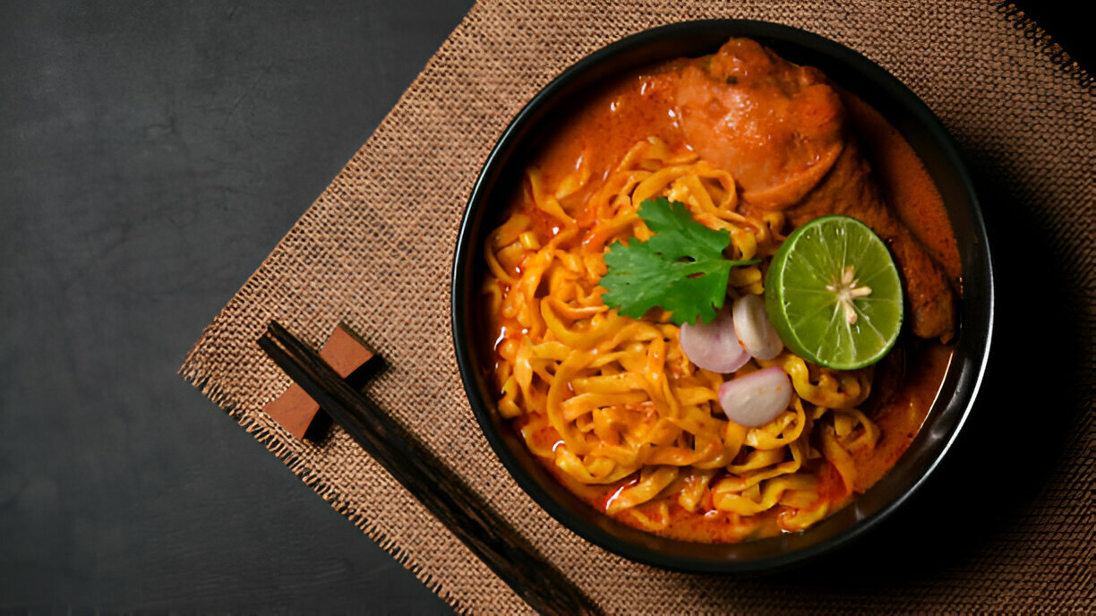 A bowl of rich chicken curry noodles topped with cilantro, lime, and shallots.