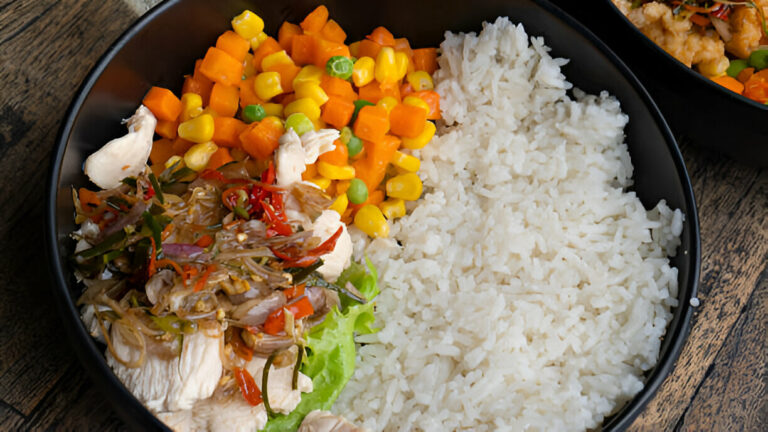 A colorful bowl containing rice, chicken, mixed vegetables, and a green lettuce leaf.