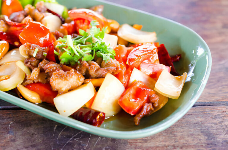 A close-up view of a colorful stir-fry dish featuring meat, vegetables, and herbs served in a green dish.