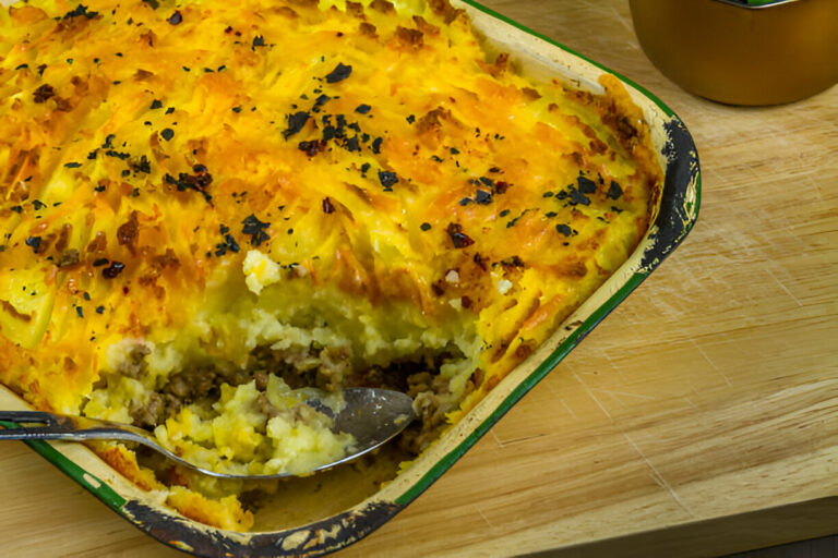 A delicious serving of shepherd's pie in a baking dish, showcasing a golden-brown potato crust with a scoop taken out to reveal the meat filling.