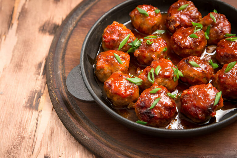 A close-up of savory meatballs topped with green onions in a black skillet.