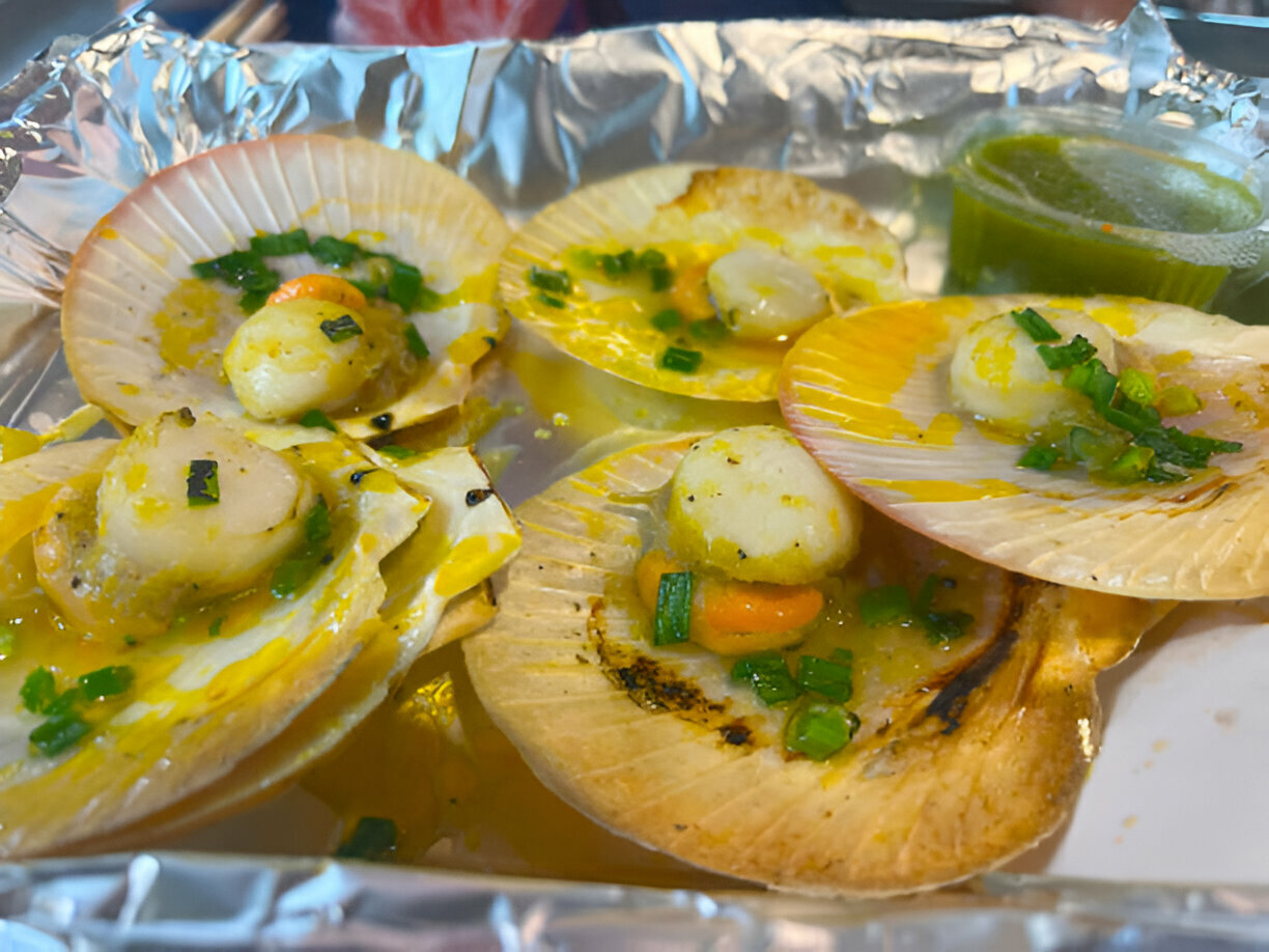 Grilled scallops served in their shells with chopped green onions and sauce.