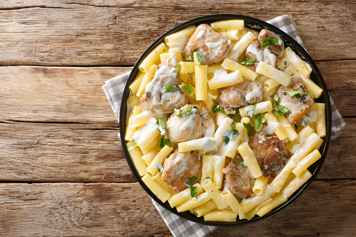 Plate of creamy chicken pasta with large rigatoni and herbs on a wooden table