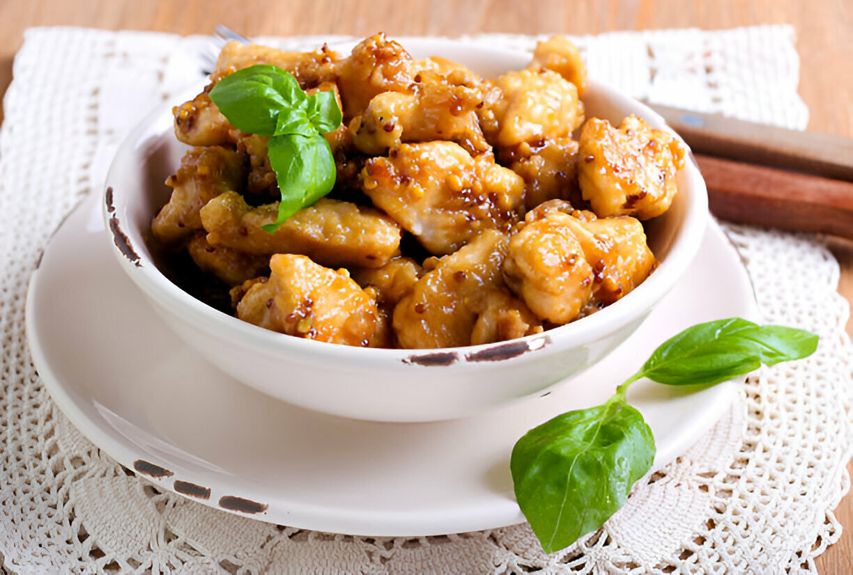 A bowl of golden, glazed chicken pieces garnished with fresh basil leaves.