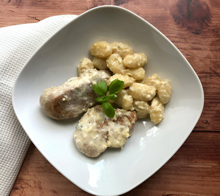 A plate of creamy gnocchi and sliced chicken garnished with fresh basil.