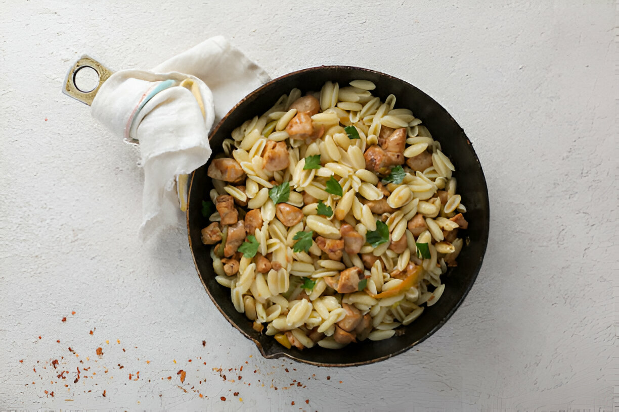 A cast iron skillet filled with pasta and chicken pieces, garnished with fresh cilantro on a light background.