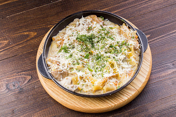 A creamy dish served in a black skillet, topped with cheese and herbs, placed on a wooden board.