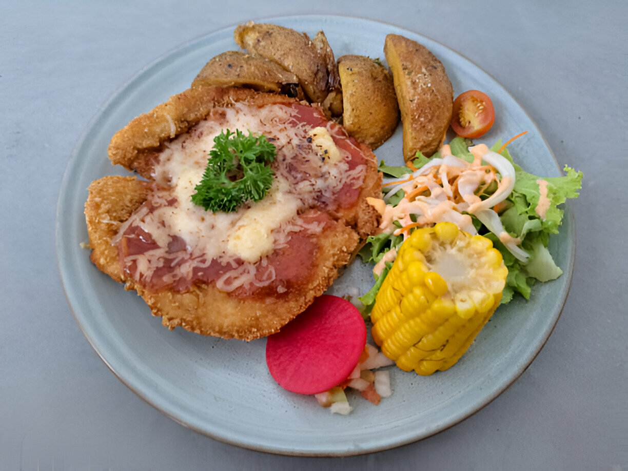 A plate of fried chicken topped with cheese, accompanied by corn, salad, and potato wedges.