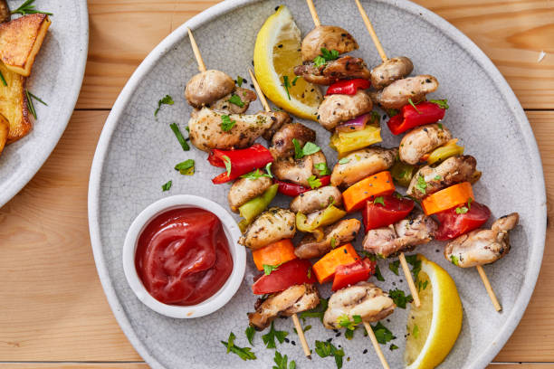 A plate of grilled chicken kebabs with vegetables and a side of ketchup.