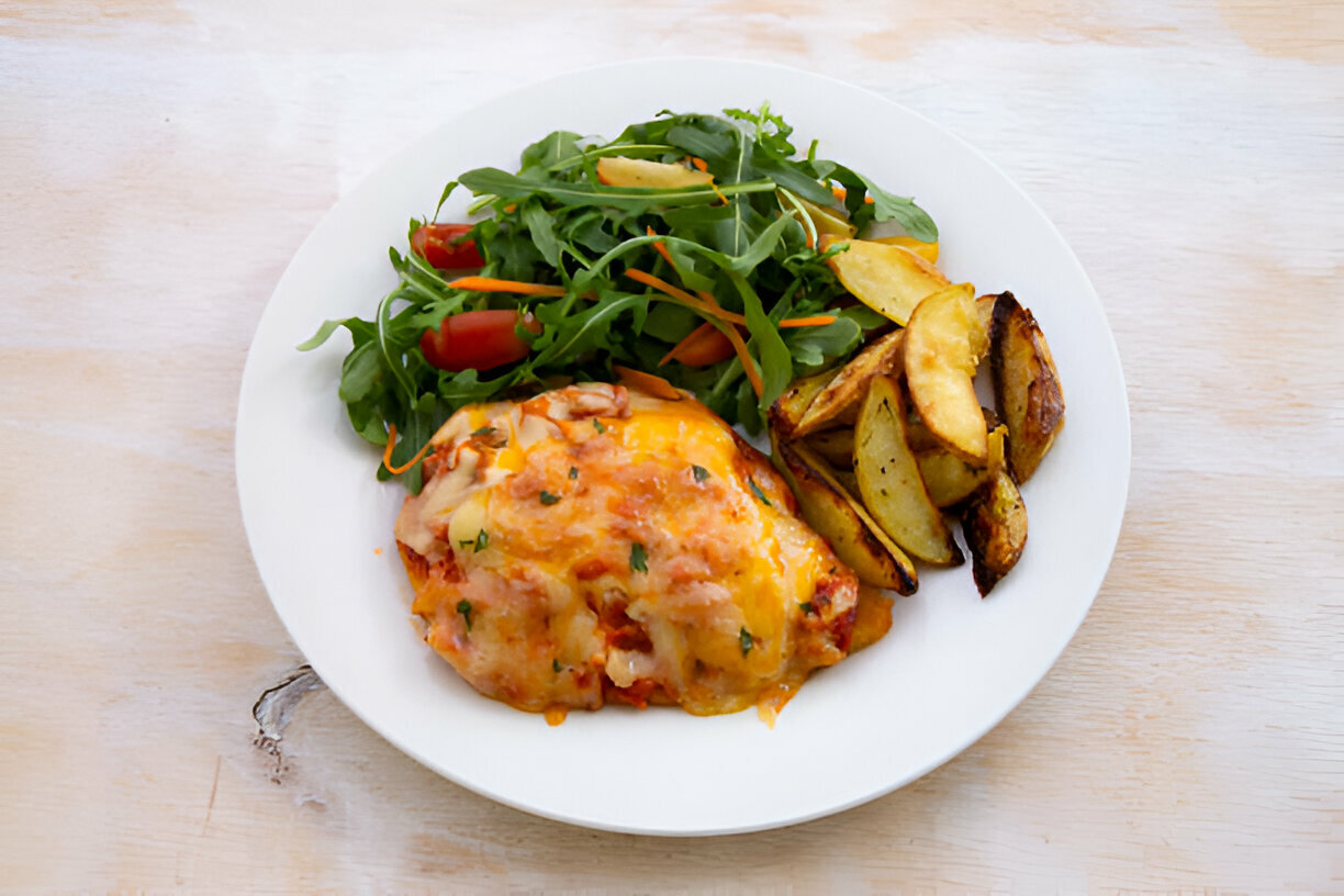 A plate of baked chicken topped with melted cheese, served with a side of roasted potatoes and a fresh salad of arugula, cherry tomatoes, and carrots.