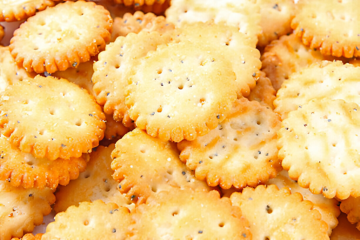 A close-up of a pile of round, crispy crackers with a golden-brown hue and a scalloped edge.