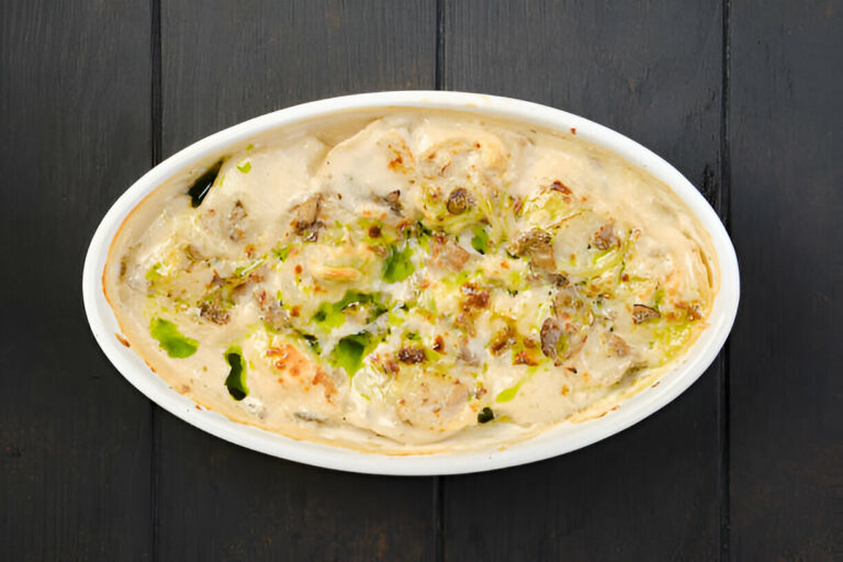 A creamy dish with layers of vegetables and possibly meat, baked until golden brown in a white oval casserole dish.