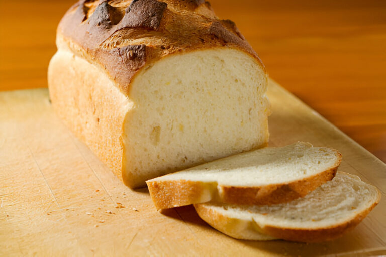 A freshly baked loaf of bread with slices cut from it on a wooden cutting board.