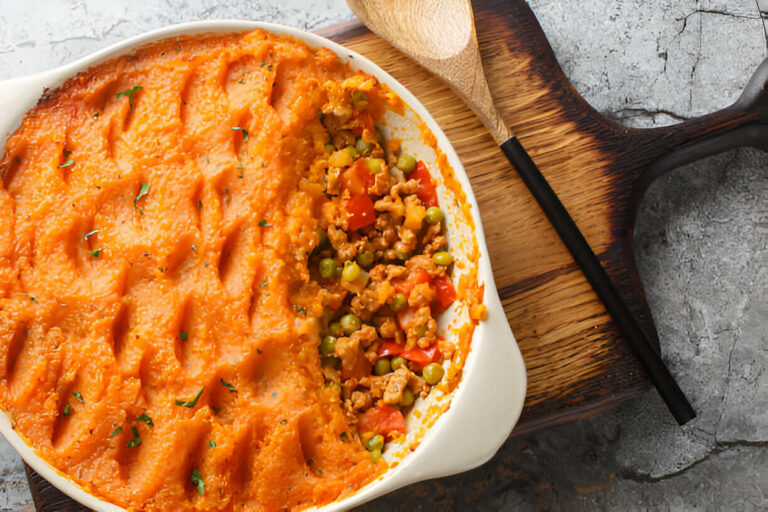 A delicious sweet potato shepherd's pie served in a white dish with a wooden spoon beside it.