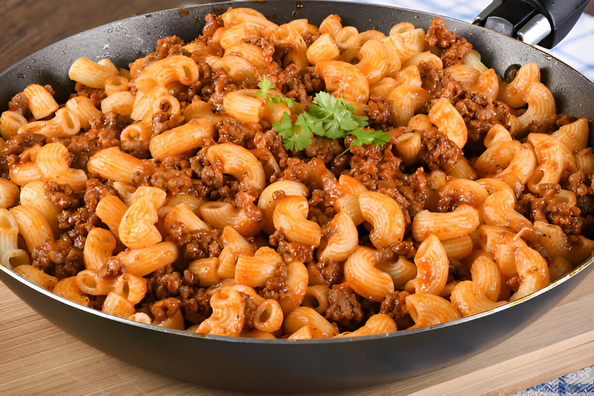 A large skillet filled with elbow macaroni mixed with ground beef in a savory tomato sauce, garnished with fresh cilantro.