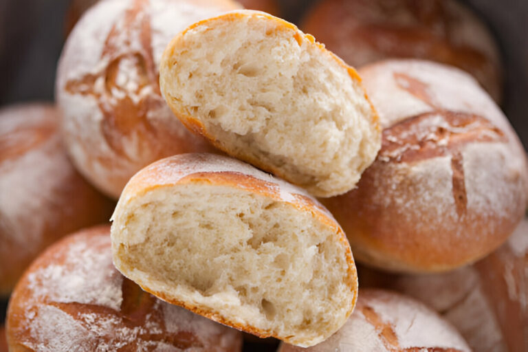 Freshly baked bread rolls placed on top of one another, with one cut in half to show the soft interior and crusty exterior.