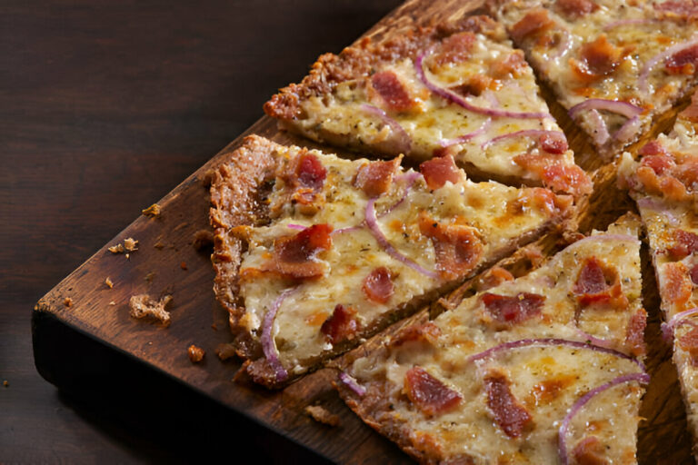 A freshly baked pizza with crispy edges, topped with bacon and red onion, cut into slices on a wooden board.