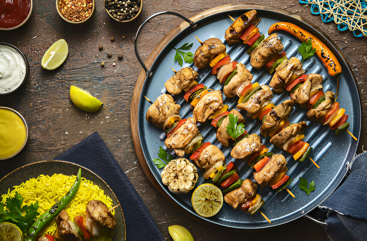 A platter of grilled chicken skewers with colorful vegetables, accompanied by sauces and sides.