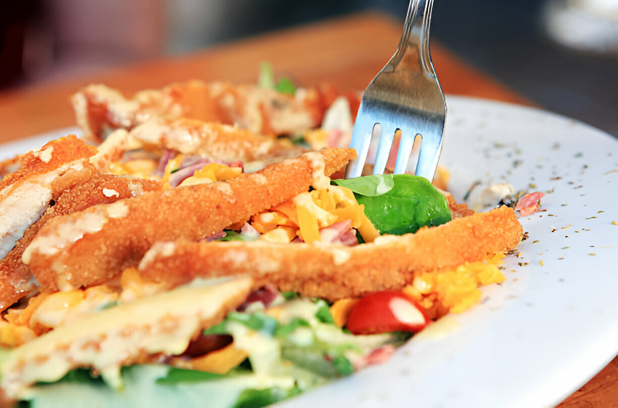 A close-up of a plate featuring a colorful salad topped with crispy chicken strips and a fork ready to serve.