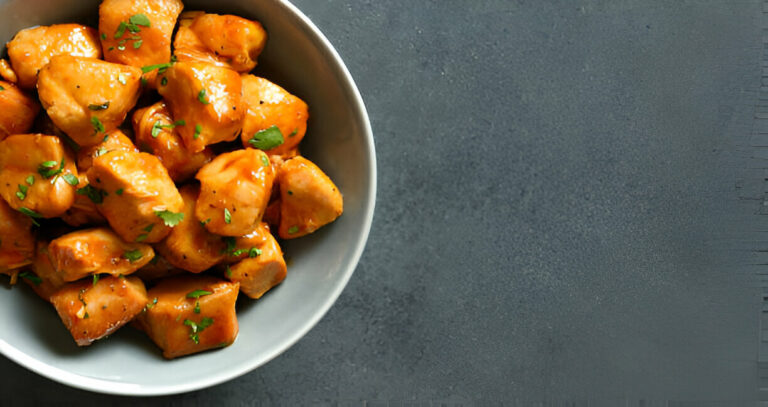 A bowl of glazed chicken pieces sprinkled with fresh herbs.