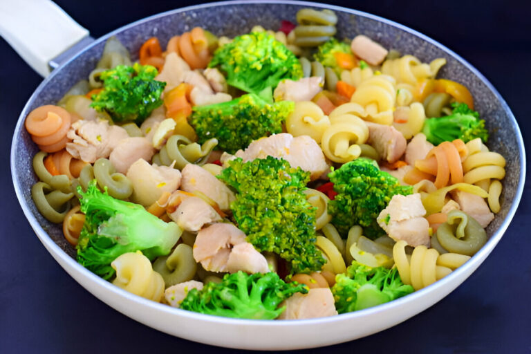 A colorful dish of pasta with chicken and broccoli in a pan.