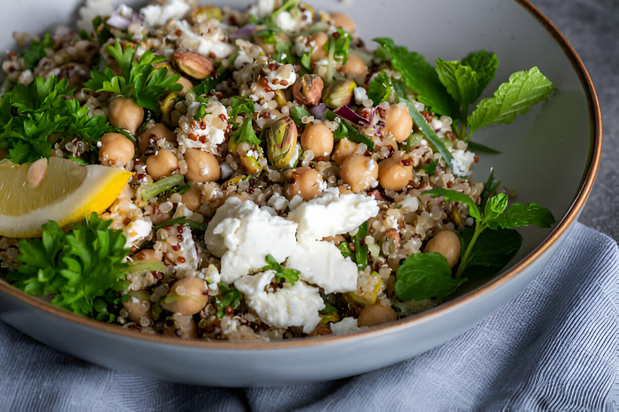 A colorful quinoa salad with chickpeas, nuts, and fresh herbs, garnished with lemon slices.