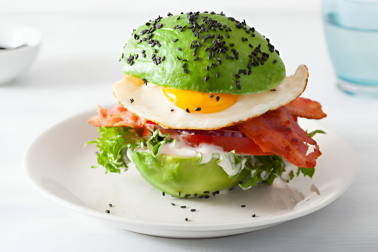 A delicious egg and bacon sandwich made with lettuce and avocado, topped with black sesame seeds.