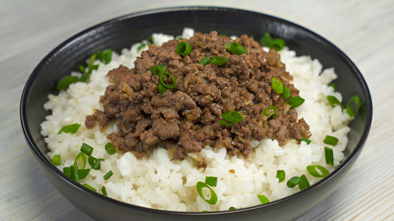 A black bowl filled with fluffy white rice topped with browned ground meat and green onions.