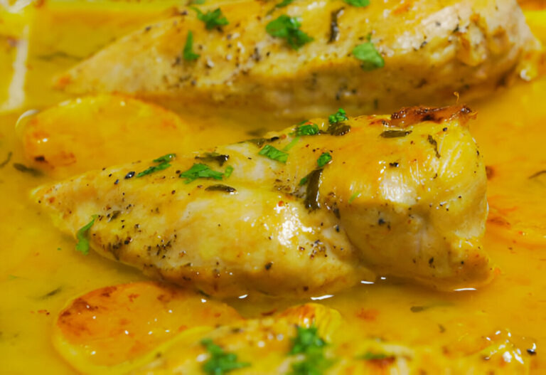 Close-up of a dish featuring cooked chicken fillets in a yellow sauce, garnished with herbs.