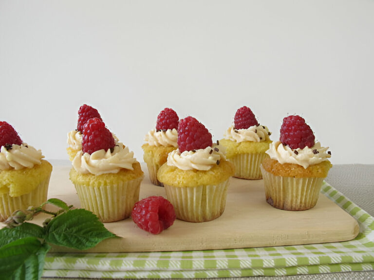 A plate of delicious cupcakes topped with frosting and fresh raspberries on a wooden board.