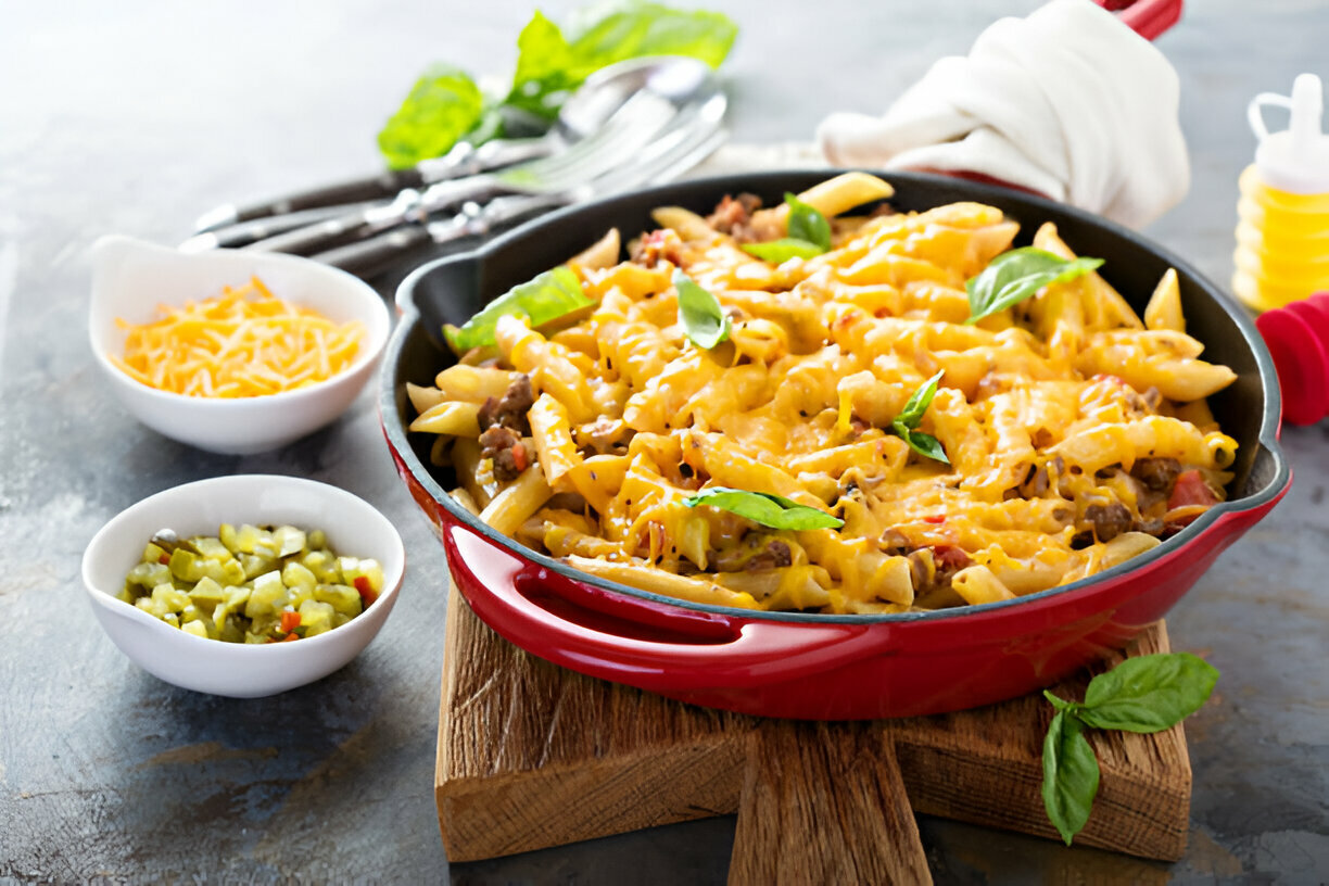 A delicious serving of baked pasta with melted cheese, topped with fresh basil leaves, served in a red skillet on a wooden board.