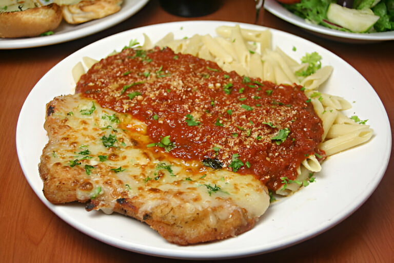 A plate of pasta served with meat topped with marinara sauce and herbs.