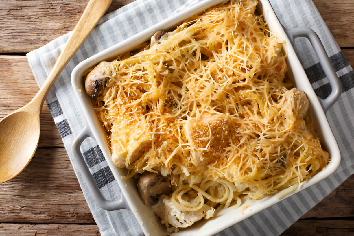 A baked spaghetti dish topped with golden cheese in a white casserole dish on a striped napkin.