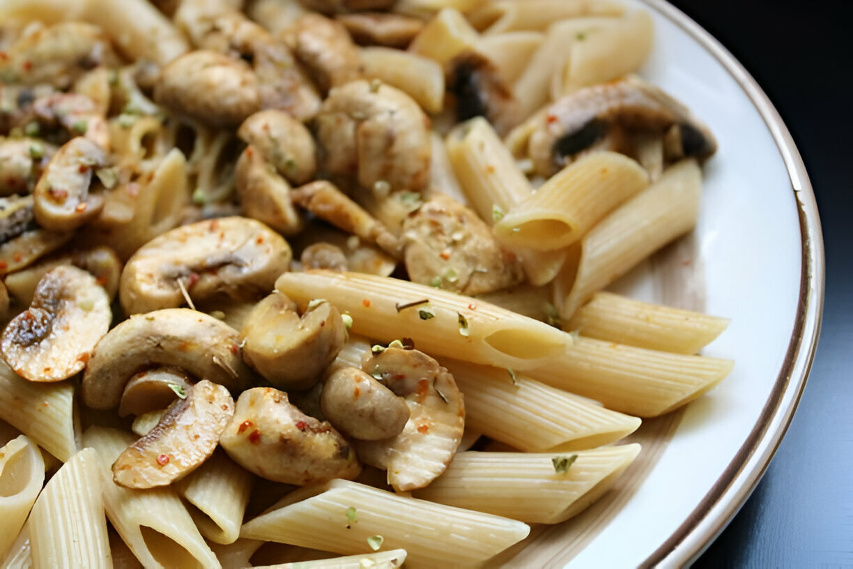 A close-up of a plate of pasta with sautéed mushrooms and seasonings.