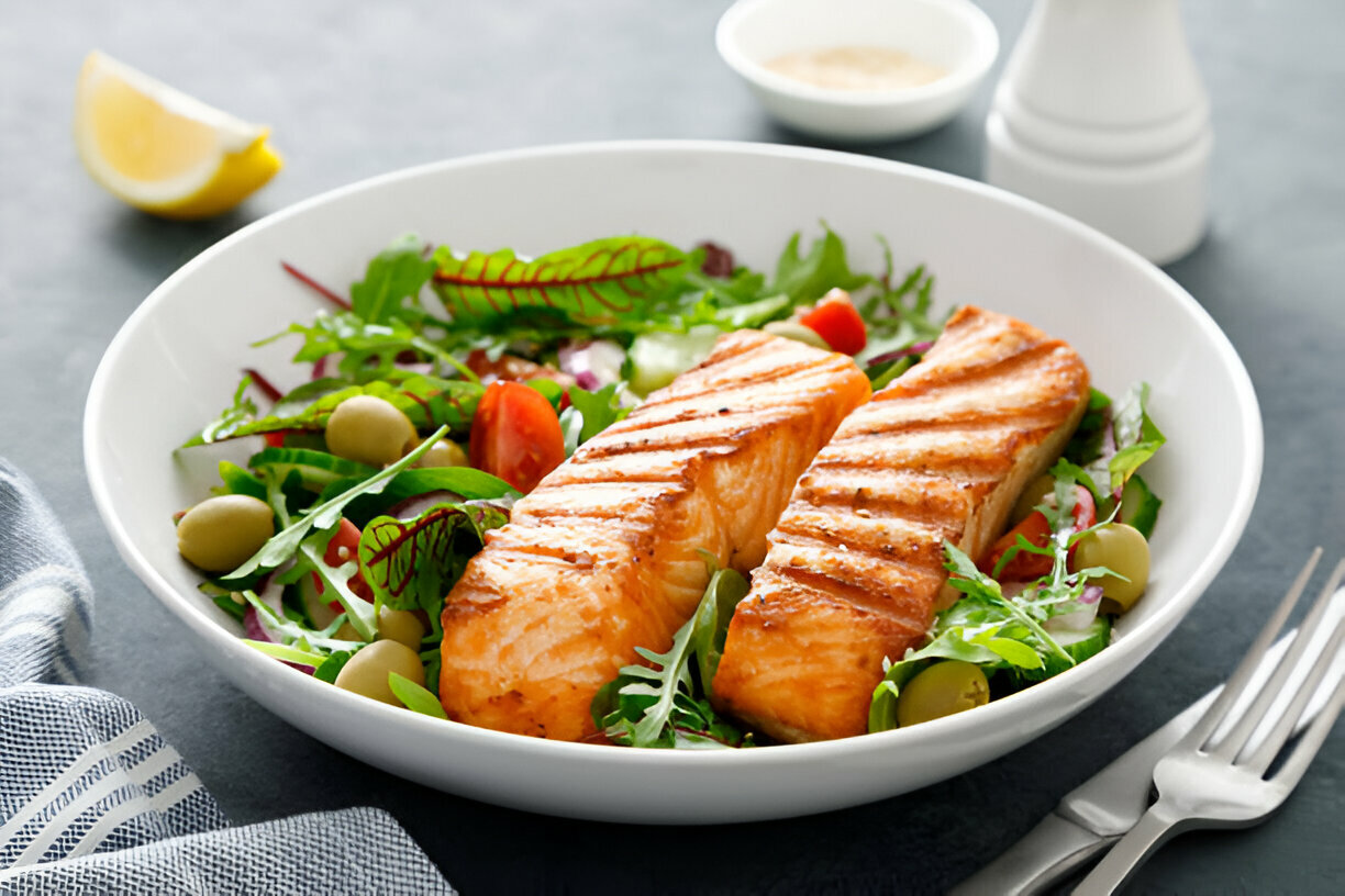 A delicious plate of grilled salmon fillets served on a bed of fresh salad greens with cherry tomatoes and olives.