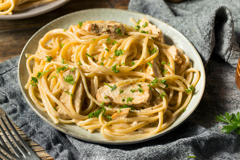 A delicious plate of creamy pasta with chicken and parsley garnished, served on a grey background.