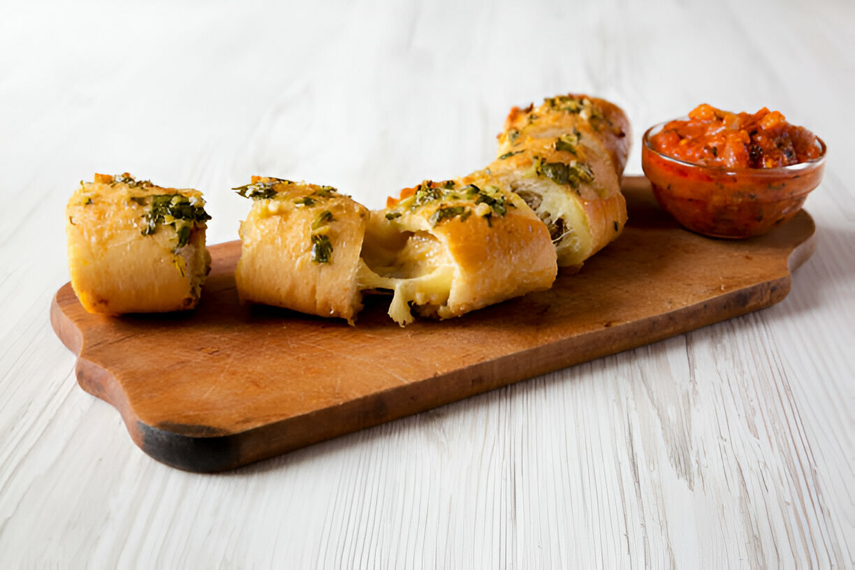 Freshly baked rolls with herbs served on a wooden board alongside a bowl of spicy sauce.