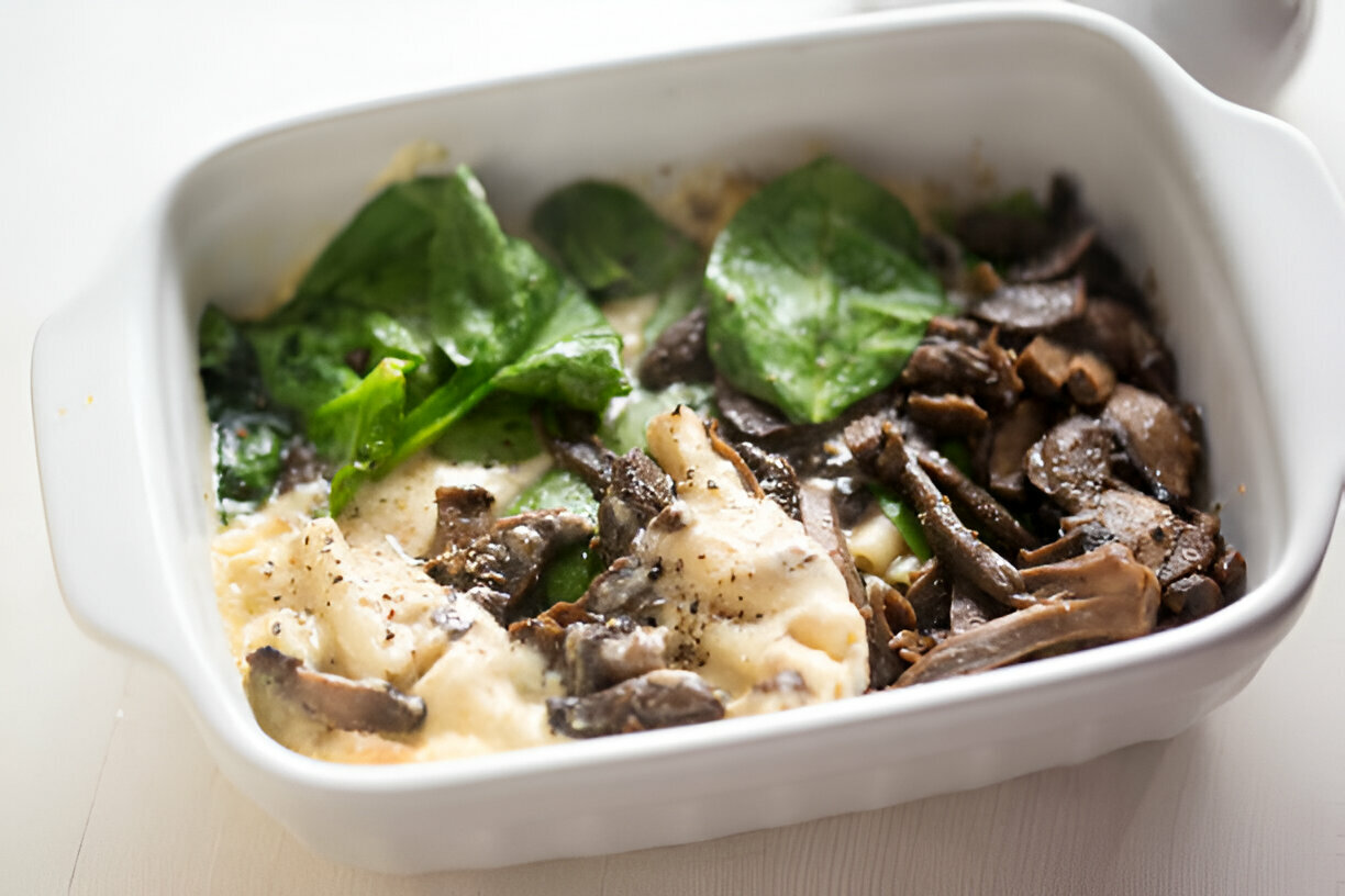 A baked dish containing spinach and mushrooms with creamy sauce and mashed potatoes.