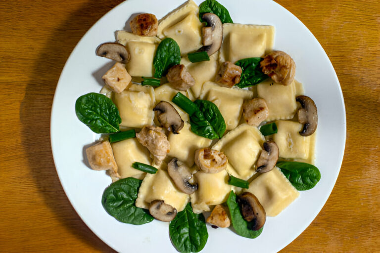 A plate of ravioli with mushrooms, spinach, and diced chicken