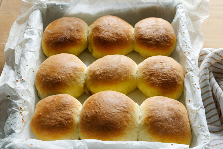 Freshly baked dinner rolls in a tray lined with parchment paper.