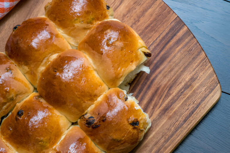 A freshly baked tray of soft buns with a shiny golden crust on a wooden cutting board.