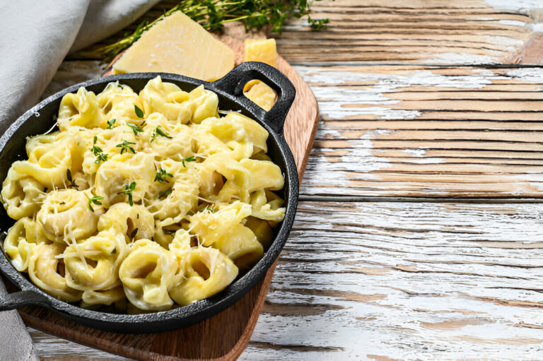 A cast iron skillet filled with creamy pasta topped with shredded cheese and fresh herbs.