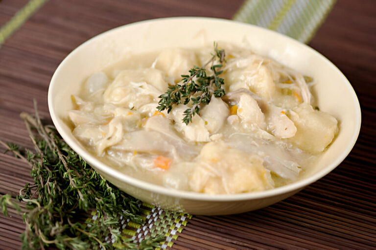 A bowl of chicken and dumpling soup garnished with thyme on a wooden surface.