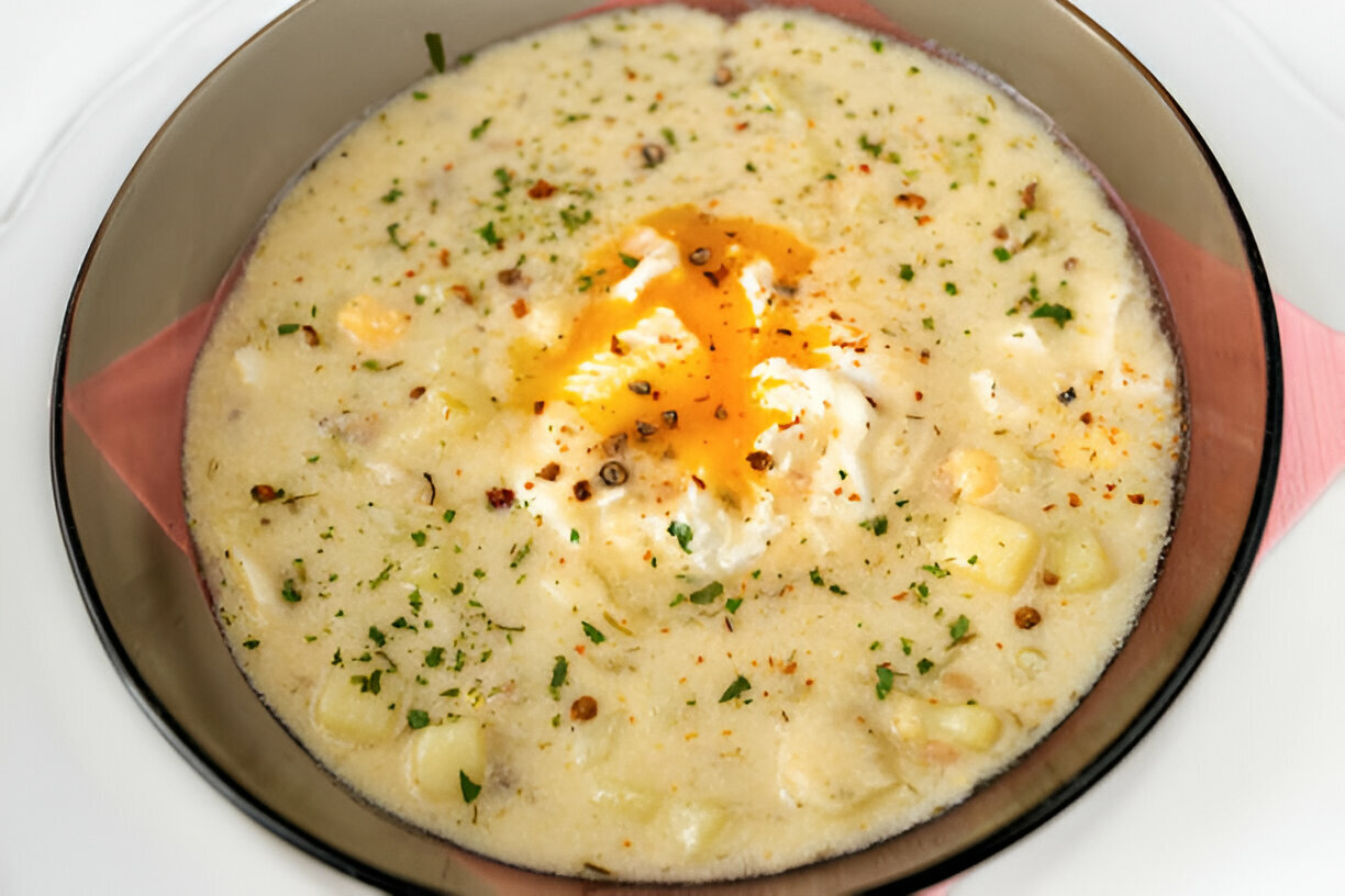 A bowl of creamy soup with a dollop of yogurt and a drizzle of yellow oil, garnished with herbs and spices.