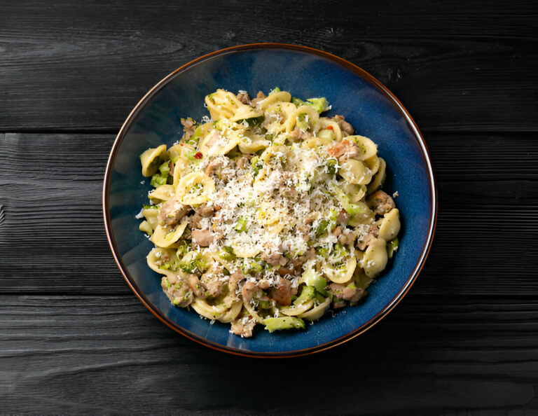 A delicious bowl of pasta with creamy sauce, topped with grated cheese and a mix of savory ingredients.